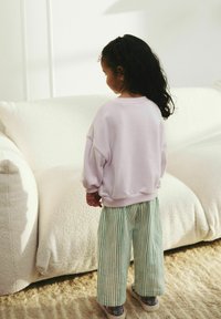 Fioletowy oversize'owy sweatshirt z opadającymi ramionami, zestawiony z zielono-białymi spodniami w szerokie paski. Miękkie tekstury, swobodny krój.