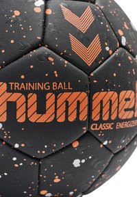 Svart träningsboll med orange detaljer, sexkantiga paneler med splash-mönster och texturerad yta för grepp. Logotypen är tydligt synlig.