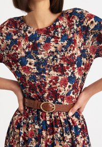 Robe à motif floral beige, avec des nuances de rouge et de bleu. Elle a des manches courtes et une ceinture marron texturée avec une boucle ovale dorée.