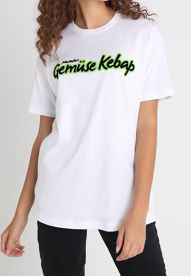 Bílý bavlněný tričko se zeleno-černým grafickým textem "Gemüse Kebap" na přední straně. Krátké rukávy a volný střih.