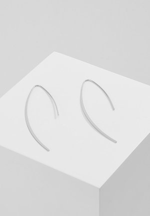 Pendientes de aro plateados con un diseño alargado y curvado. Hechos de metal, con un acabado suave y un estilo minimalista, reposando sobre un pedestal blanco.