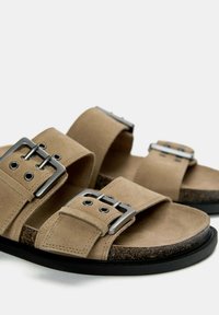Samtbraune Sandalen mit zwei breiten Riemen, silbernen Schnallen und einer strukturierten Korkfußbett. Schwarze Gummisohle mit kontrastierenden Steppnähten.