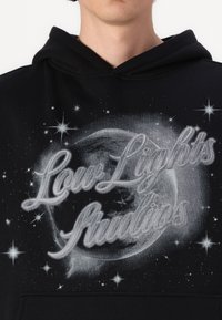Felpa nera con cappuccio caratterizzata da una stampa grafica che rappresenta un globo circondato da stelle. Il testo "Low Lights Studios" è in argento, con una texture morbida.