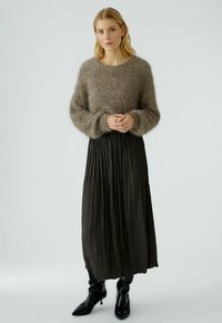 Losse, fuzzy bruine trui met lange mouwen, gecombineerd met een zwarte, geplooide midi-jurk en zwarte, puntige enkellaarsjes.