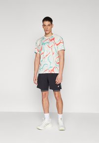 Kortermet, mintfarget skjorte med abstrakte mønstre i korall og turkis, kombinert med svarte treningsshorts og hvite joggesko.