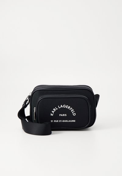 Sac bandoulière en nylon noir avec texte et logo blancs, doté d'un compartiment zippé et d'une sangle ajustable. Forme rectangulaire avec texture lisse.