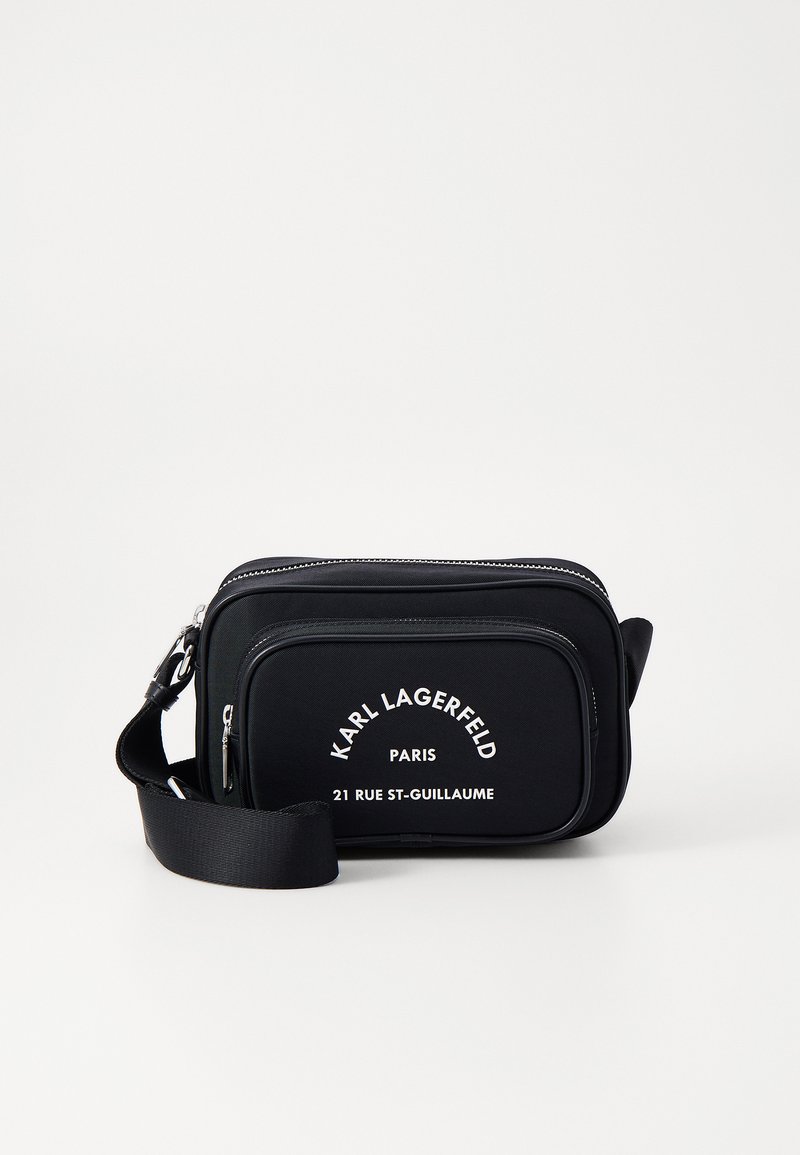 Borsa a tracolla nera in nylon con testo e marchio bianchi, dotata di un compartimento con zip e cinturino regolabile. Forma rettangolare con superficie liscia.