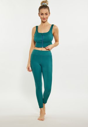 Teal sportos crop top, cipzárral és vastag pántokkal, melyet passzoló, magas derekú leggings-szel párosítottak. Sima, rugalmas anyag az egész területen.