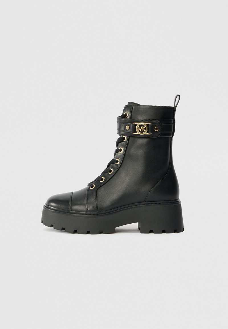 Black leather ankle boot with a thick platform sole, gold eyelets, and a decorative strap featuring a gold logo accent.
