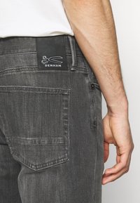 Denham gray denim jeans with a black leather brand patch featuring a scissor logo, straight cut design, and back pocket detailing.