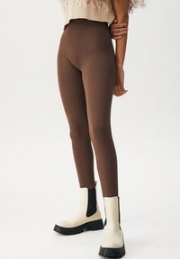 Brune ribbede leggings lavet af strækbart materiale, parret med cremefarvede ankelstøvler med sorte sidedele og en chunky sål.