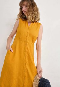 Sleeveless yellow linen dress with a V-neck, button front, and side pockets. Features a textured hem with a woven accent.
