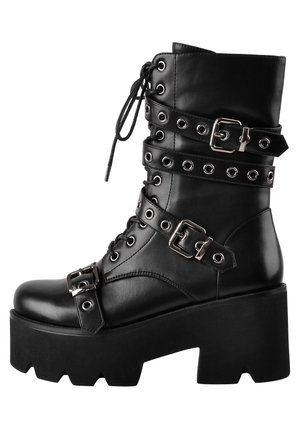 Black faux leather knee-high lace-up boot with metal buckles, grommets, and a chunky heel. Features a textured sole and layered strap design.