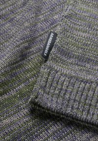 Knitted sweater in green, gray, and purple stripes. Features ribbed cuffs and a label reading "ARMEDANGELS." Soft, textured fabric.