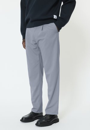 Pantalon gris clair à coupe droite, avec des poches avant et une texture lisse. Associé à des mocassins noirs et un pull marine.