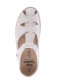 White suede sandal with an open toe design, crisscross straps, and cut-out details. Features a textured footbed and stitched edges.