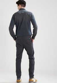 Cămașă din denim închis cu un yoke structurat și mâneci lungi, asortată cu pantaloni slim-fit de culoare cărbune și adidași bej, cu detalii minime.