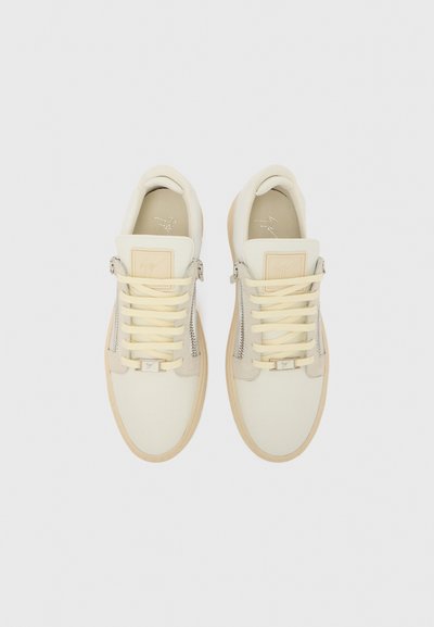 Baskets blanches avec dessus en cuir lisse, accents jaunes, côtés zippés et semelles en caoutchouc texturées de couleur tan. Comprend des écussons de logo bien visibles.