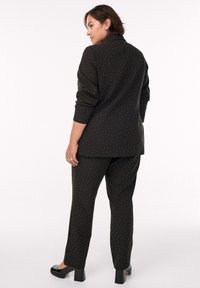 Black suit with small white polka dots; structured blazer with notch lapels and matching straight-leg pants; paired with black block-heeled shoes.