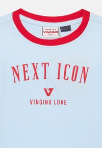 Světle modré tričko s červeným žebrovaným límcem. Na přední straně se nachází výrazný červený nápis "NEXT ICON" a pod ním "VINGINO LOVE". Měkká bavlněná textura.
