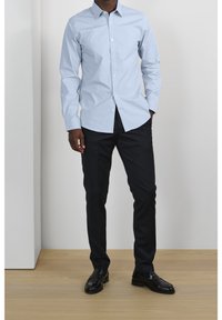 Ljusblå skjorta med knappar och långa ärmar, i kombination med mörka, skräddarsydda byxor och svarta läderskor. Slät tygfinish.