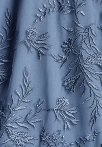 Tela azul con intrincados bordados florales en diferentes tonos de azul. La textura presenta puntos elevados y formas orgánicas fluidas.