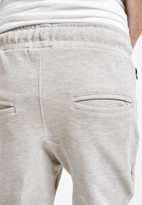Gray sweatpants featuring a soft texture, elastic waistband, and two rounded back pockets with subtle stitching details.