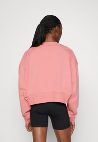 Sweatshirt rose coupé avec un col rond et des épaules tombantes, fabriqué en tissu doux. Porté avec un short de sport noir.