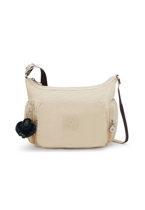 Sac bandoulière beige avec poche zippée à l'avant, sangle sombre ajustable, compartiments latéraux et porte-clés gorille noir et duveteux attaché.