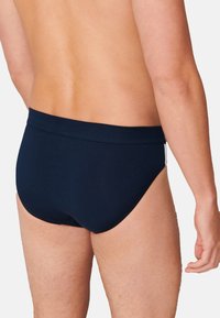 Bañador azul marino fabricado en tela suave. Cuenta con una cinturilla lisa y un ajuste ceñido con una cobertura mínima en la parte trasera.