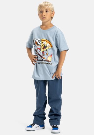 Lichtblauw katoenen T-shirt met een grafiek van een cartoonpizza op een skateboard. Donkerblauwe broek, witte schoenen met blauwe accenten en zwarte veters.