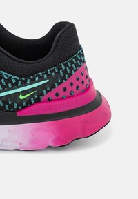 Gros plan sur le talon arrière d’une chaussure de course Nike React noire, rose et turquoise avec une semelle amortissante et une tige texturée.