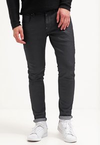 Jeans negros de corte ajustado con una textura suave, brillo sutil y dobladillos enrollados, combinados con zapatillas blancas.