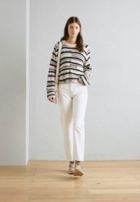 Suéter de punto a rayas en crema, negro y beige; pantalones rectos blancos; sneakers beige; diseño minimalista sobre un fondo sencillo.