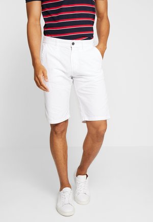 Shorts en coton blanc avec poches avant et fermeture à bouton, associés à un polo rayé bleu marine et rouge et des baskets blanches.