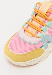 Baskets colorées avec une tige en maille rose et des accents en daim jaune et bleu, des lacets orange contrastants et une étiquette bien visible.