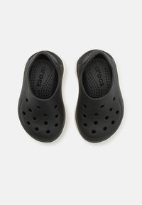 Svart gummiträskor med ventilationshål, strukturerad innersula, vit sula och "CROCS"-logotyp tryckt inuti.