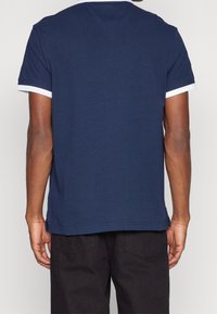 T-shirt bleu marine avec des bordures blanches au niveau du col et des manches, en coton, avec une coupe droite et une texture lisse.
