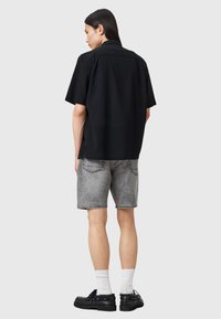 Svart kortärmad skjorta med en avslappnad passform, kombinerad med hög midja i ljusgr�å denimshorts. Svarta skor med tjocka sulor fulländar looken.