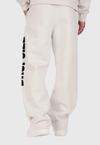 Brīvi pieguļošas, krēmkrāsas kokvilnas sporta bikses ar lielu melnu apdrukātu logo pa kreiso pusi. Elastīgs jostasvieds un aproces.