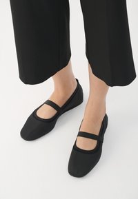 Ballerine nere in materiale liscio, con punta rotonda e una fascia a contrasto sul collo del piede. Suola piatta, design minimalista.