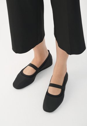 Svarte flater laget av glatt materiale, med rund tå og en kontrasterende stropp over vristen. Flatt såle, minimalistisk design.