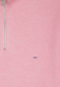 Pull en maille rose avec un motif texturé, fermeture éclair en argent et un petit logo violet dans le coin inférieur droit.