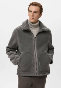 Grijze fleecejas met een ritssluiting aan de voorkant, grote zakken en een kraag. Zachte textuur met een ontspannen pasvorm en minimale stikdetails.