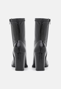 Sorte ankelstøvler i laklæder med chunky hæl, der har lynlåslukning og en glat, blank overflade på overdelen.