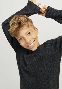 Un pull en tricot côtelé gris foncé avec un col rond et des manches allongées, porté par un enfant souriant avec des cheveux courts et ondulés.