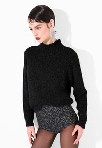 Maglione nero lavorato a maglia con collo alto e polsini a coste, abbinato a un capo inferiore scuro con motivo testurizzato. Accessori lisci e lucidi.