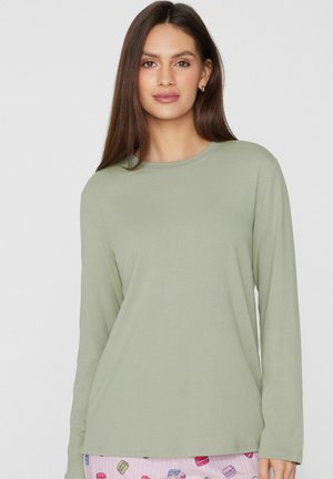 Chemise à manches longues vert clair, col rond, tissu en coton doux, coupe ajustée. Portée avec un pantalon rose à motif coloré de macarons.