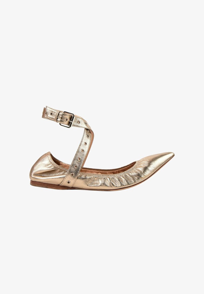 Chaussure plate pointue en or métallisé avec bride à la cheville et boucle sur fond blanc.