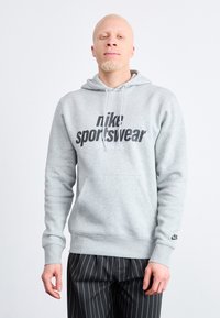 Pilkas medvilnės džemperis su dideliu juodu "nike sportswear" grafinu, su kapuce ir kengūros kišene. Rausvos rankogaliai ir apatinis kraštas.